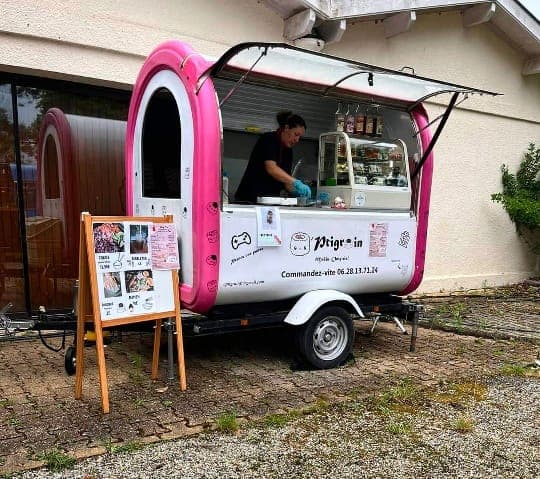 Aurélie en train de cuisiner dans la roulotte rose et blanche du O’ptigrain, le menu affiché sur un chevalet devant.